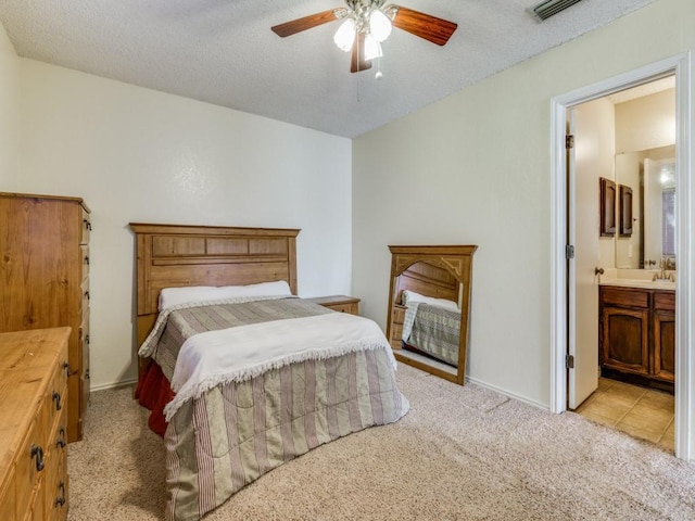 bedroom featuring visible vents, a textured ceiling, ensuite bath, baseboards, and light colored carpet