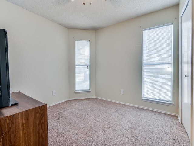 carpeted empty room featuring a textured ceiling and baseboards