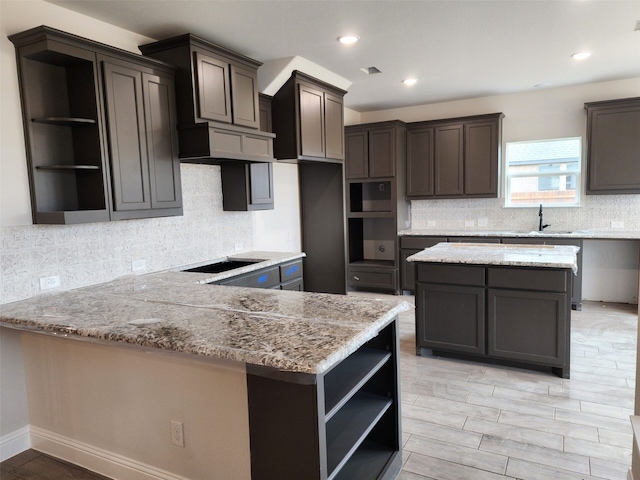 kitchen with cooktop, light stone counters, dark brown cabinets, and sink