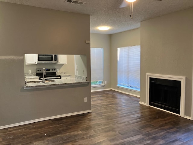 kitchen with appliances with stainless steel finishes, light stone countertops, a textured ceiling, white cabinets, and dark hardwood / wood-style flooring