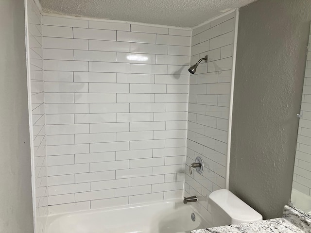 bathroom featuring tiled shower / bath, a textured ceiling, and toilet