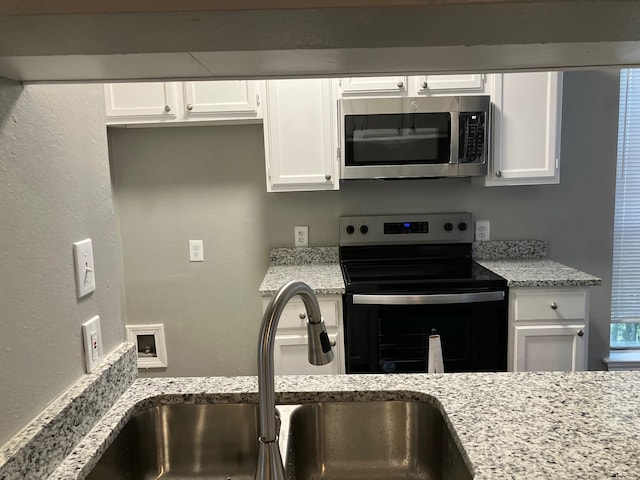 kitchen with appliances with stainless steel finishes, light stone counters, white cabinetry, and sink