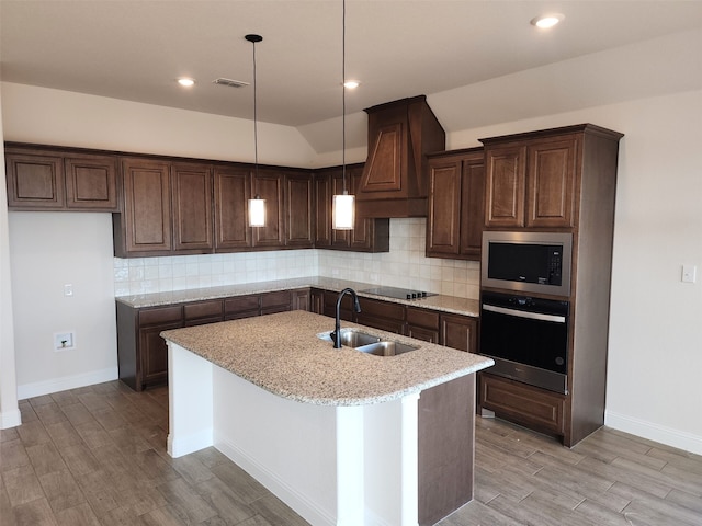 kitchen with sink, premium range hood, decorative light fixtures, a kitchen island with sink, and appliances with stainless steel finishes