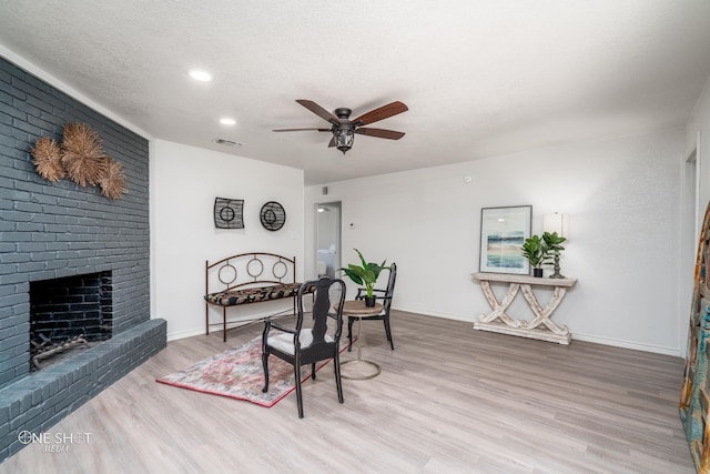 dining room with a textured ceiling, ceiling fan, wood-type flooring, and a fireplace