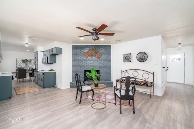 living room with ceiling fan, light hardwood / wood-style flooring, a textured ceiling, and a brick fireplace