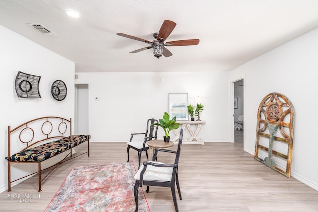 living area with a textured ceiling, light hardwood / wood-style floors, and ceiling fan