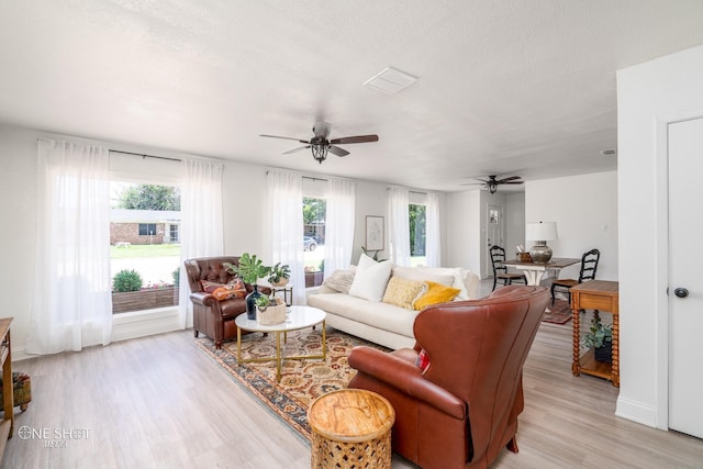 living room featuring a textured ceiling, light wood-type flooring, and ceiling fan