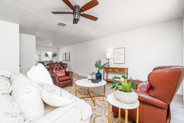 living room with ceiling fan, a textured ceiling, and light wood-type flooring