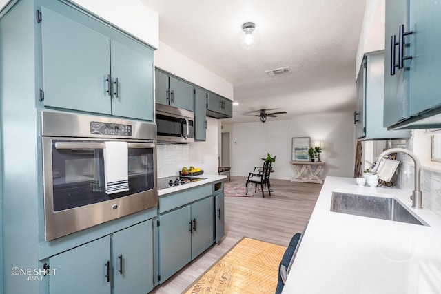 kitchen with backsplash, stainless steel appliances, blue cabinets, ceiling fan, and sink