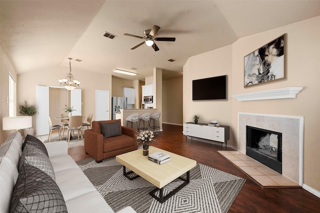 living room with vaulted ceiling, ceiling fan with notable chandelier, a tiled fireplace, and hardwood / wood-style floors