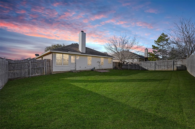 back house at dusk featuring a lawn