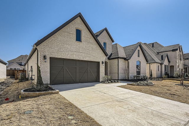 french country inspired facade featuring concrete driveway, fence, and brick siding