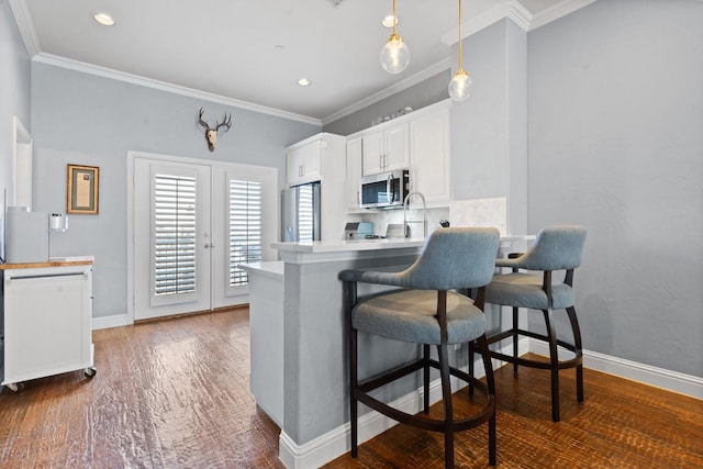 kitchen with a breakfast bar, kitchen peninsula, ornamental molding, white cabinetry, and stainless steel appliances