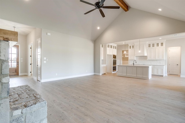 unfurnished living room featuring ceiling fan, sink, light hardwood / wood-style flooring, beamed ceiling, and high vaulted ceiling