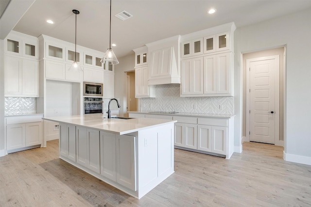 kitchen with wall oven, built in microwave, sink, a center island with sink, and white cabinetry