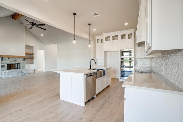 kitchen with appliances with stainless steel finishes, a kitchen island with sink, beam ceiling, pendant lighting, and white cabinetry