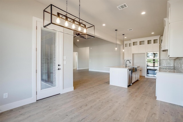 kitchen featuring white cabinetry, hanging light fixtures, stainless steel appliances, backsplash, and a center island with sink