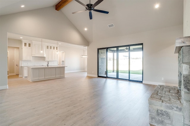 unfurnished living room with high vaulted ceiling, ceiling fan, light wood-type flooring, a fireplace, and beam ceiling