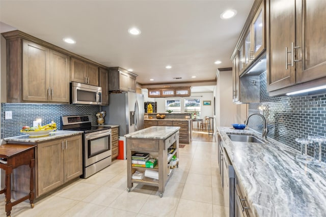 kitchen with light tile patterned flooring, sink, light stone counters, appliances with stainless steel finishes, and a kitchen island