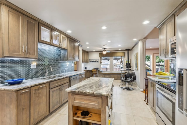 kitchen with appliances with stainless steel finishes, a center island, light stone counters, tasteful backsplash, and light tile patterned flooring