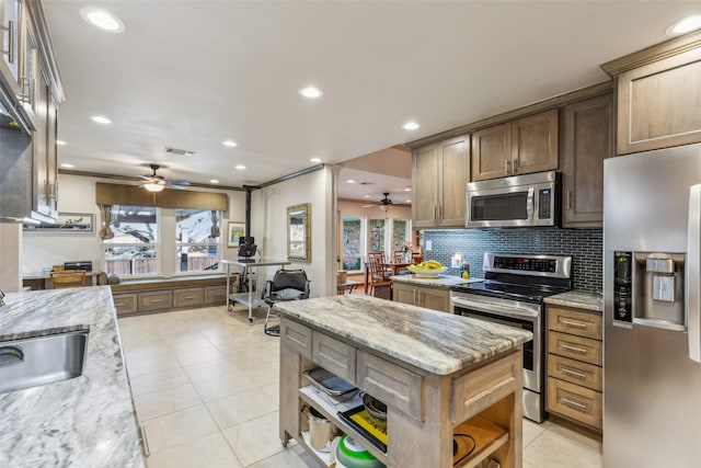 kitchen with light stone counters, backsplash, stainless steel appliances, and a center island