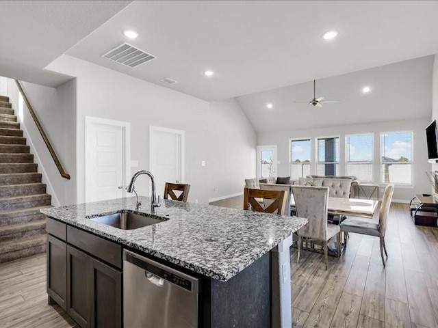 kitchen with stainless steel dishwasher, light stone counters, sink, and a kitchen island with sink