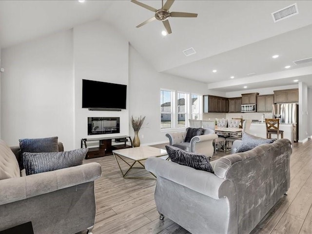 living room with light hardwood / wood-style floors, high vaulted ceiling, and ceiling fan