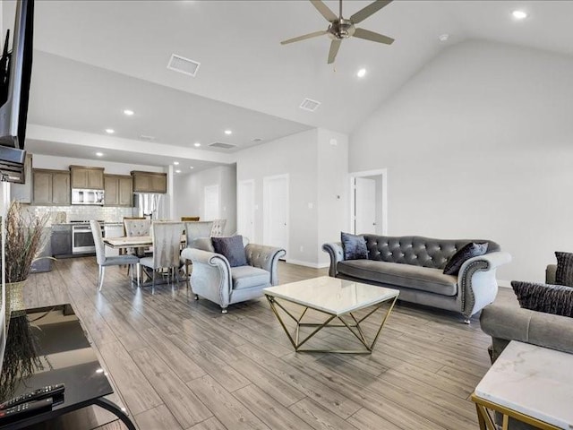 living room with light hardwood / wood-style floors, high vaulted ceiling, and ceiling fan