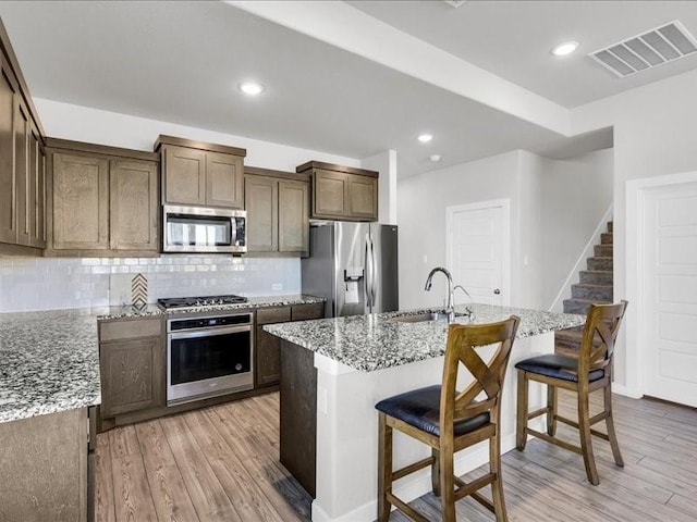 kitchen with sink, light stone counters, a kitchen island with sink, a breakfast bar, and appliances with stainless steel finishes