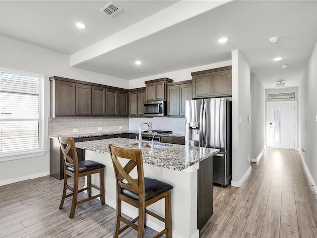 kitchen featuring light stone countertops, stainless steel appliances, a kitchen island with sink, and a breakfast bar area