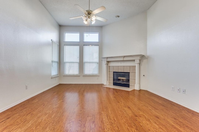 unfurnished living room featuring ceiling fan, a fireplace, light hardwood / wood-style floors, and a textured ceiling