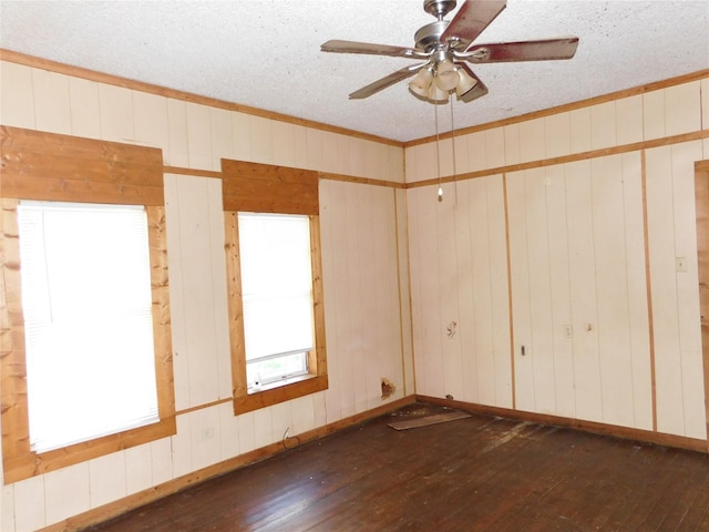 empty room with a textured ceiling, ceiling fan, crown molding, dark wood-type flooring, and wood walls