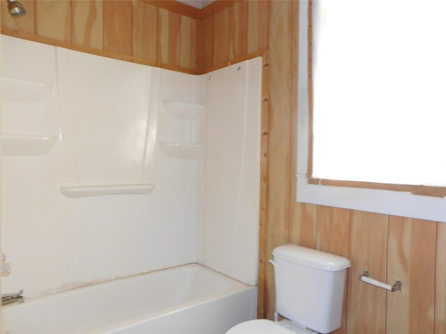 bathroom with shower / bathing tub combination, toilet, and wooden walls