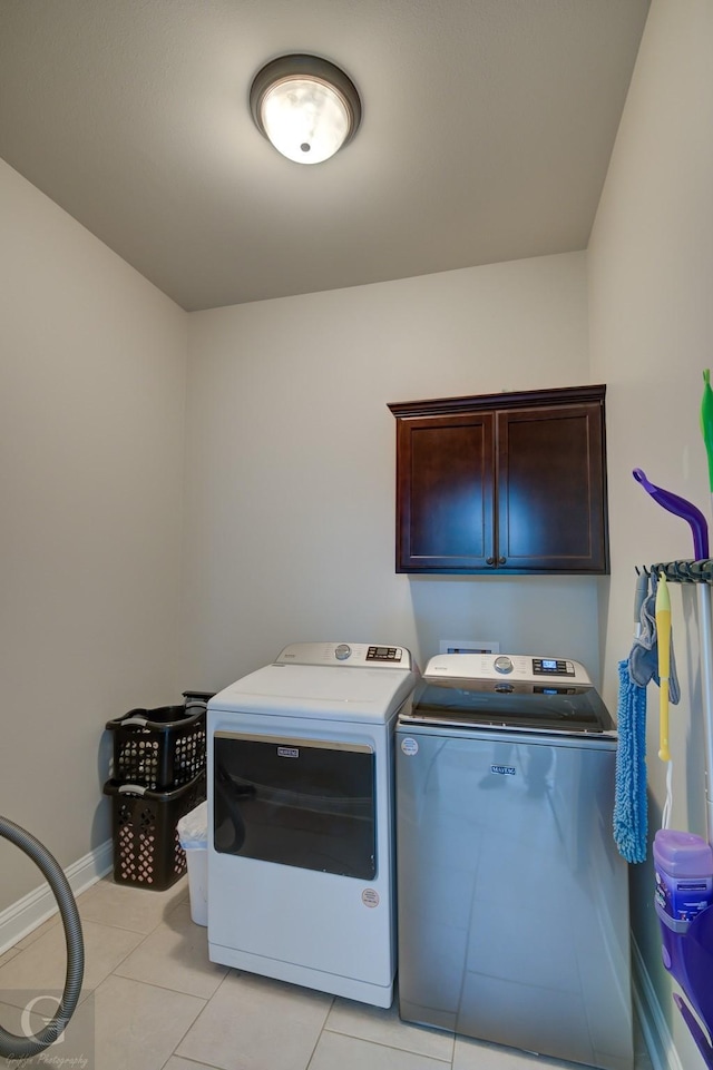 clothes washing area featuring light tile patterned flooring, cabinet space, washer and dryer, and baseboards