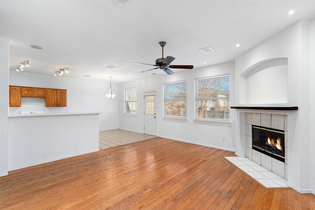 unfurnished living room with ceiling fan, light hardwood / wood-style floors, and a tiled fireplace