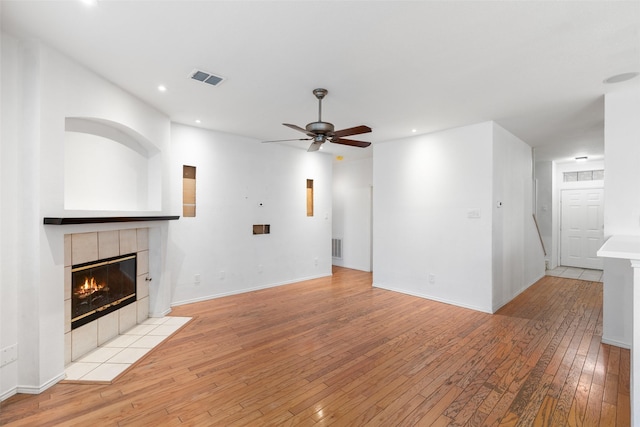 unfurnished living room featuring light wood-type flooring, ceiling fan, and a tiled fireplace