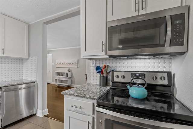 kitchen with backsplash, stainless steel appliances, white cabinets, stone countertops, and light wood-type flooring