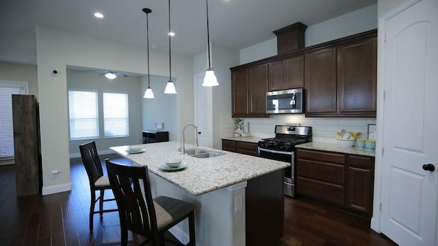 kitchen with decorative backsplash, stainless steel appliances, sink, a center island with sink, and hanging light fixtures