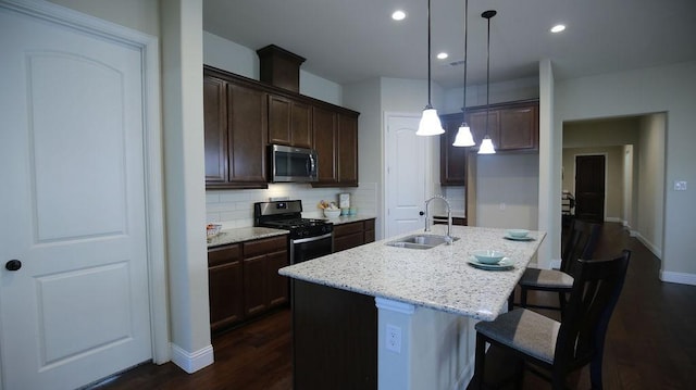 kitchen with pendant lighting, backsplash, a kitchen island with sink, sink, and stainless steel appliances