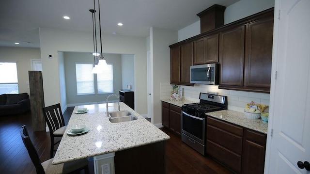 kitchen with a breakfast bar, stainless steel appliances, a kitchen island with sink, sink, and hanging light fixtures