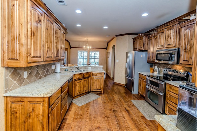 kitchen with light stone counters, wood-type flooring, hanging light fixtures, kitchen peninsula, and stainless steel appliances