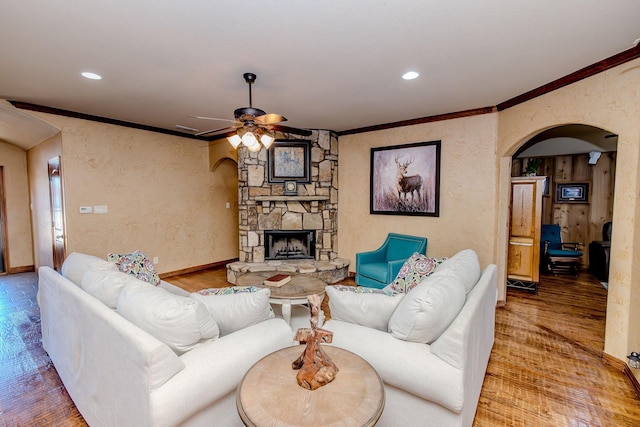 living room with ornamental molding, a stone fireplace, and wood-type flooring