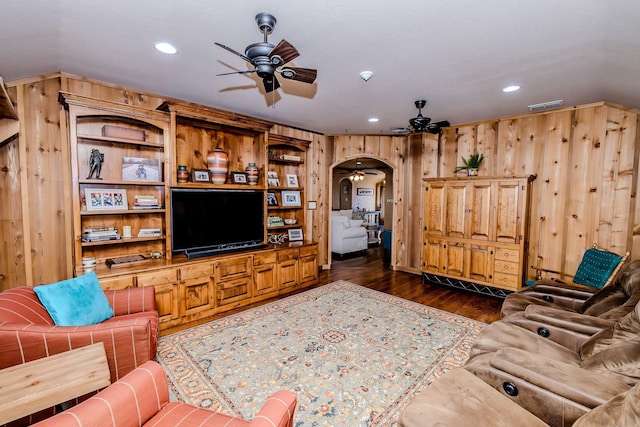 living room with dark hardwood / wood-style flooring, wooden walls, and ceiling fan