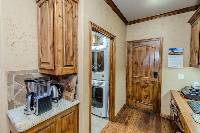 kitchen with light stone countertops, ornamental molding, stacked washer and clothes dryer, and hardwood / wood-style floors