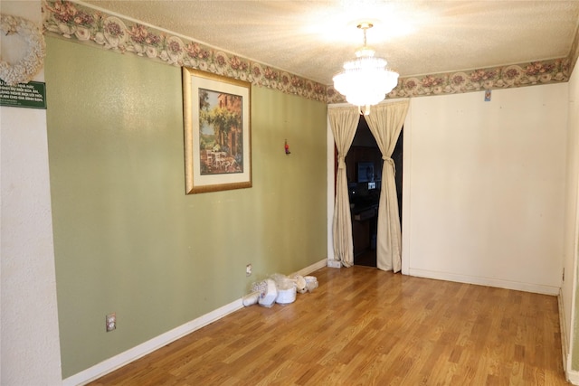 spare room with hardwood / wood-style floors, a textured ceiling, and an inviting chandelier