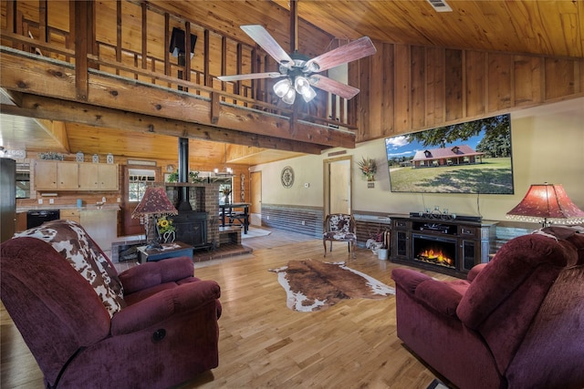 living room featuring a wood stove, ceiling fan, light hardwood / wood-style flooring, high vaulted ceiling, and wood ceiling