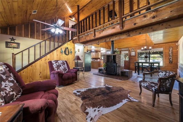 living room featuring a wood stove, high vaulted ceiling, ceiling fan with notable chandelier, wood-type flooring, and wood ceiling