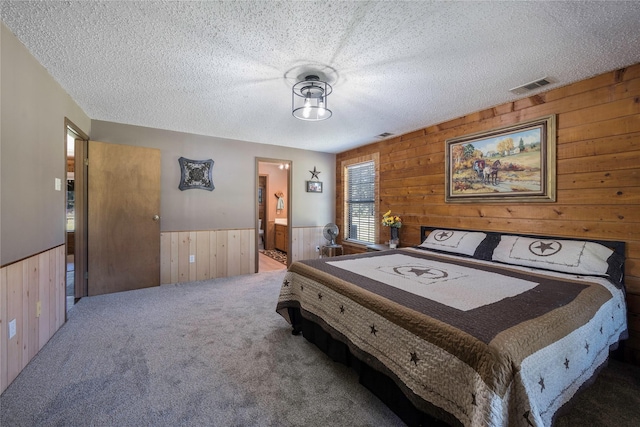 carpeted bedroom with a textured ceiling, wooden walls, and connected bathroom