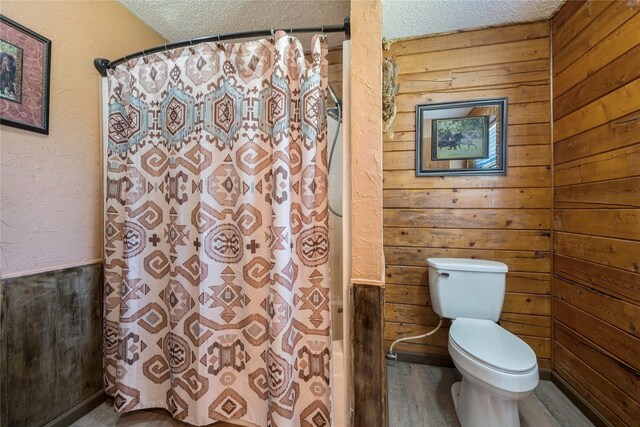 bathroom featuring hardwood / wood-style floors, a textured ceiling, toilet, and wooden walls