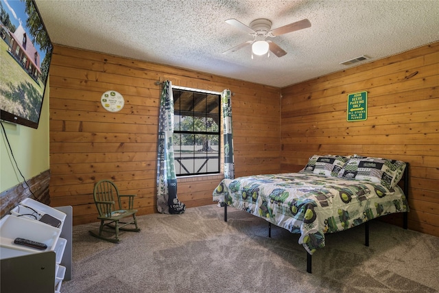 carpeted bedroom featuring a textured ceiling, ceiling fan, and wood walls